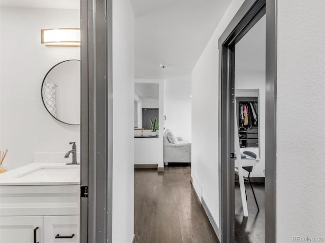 hallway featuring dark wood-style flooring, a sink, and baseboards