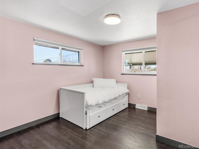 unfurnished bedroom with dark wood-type flooring, multiple windows, visible vents, and baseboards