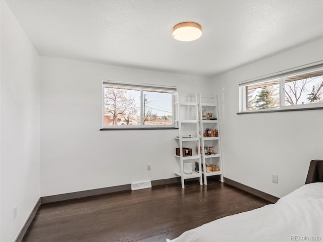 bedroom with visible vents, a textured ceiling, baseboards, and wood finished floors