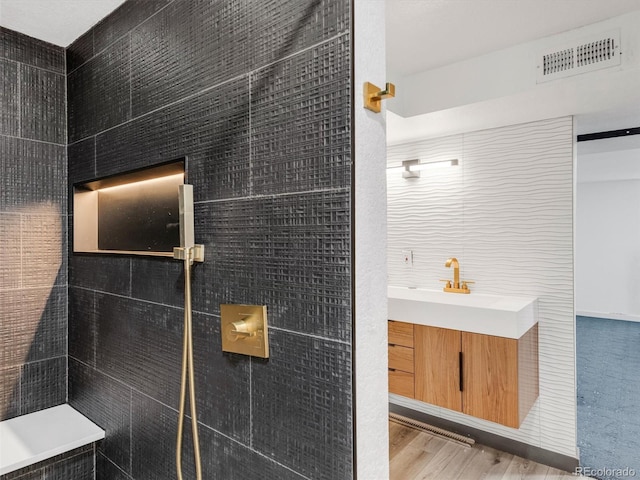 full bath featuring tile walls, visible vents, tiled shower, wood finished floors, and a sink