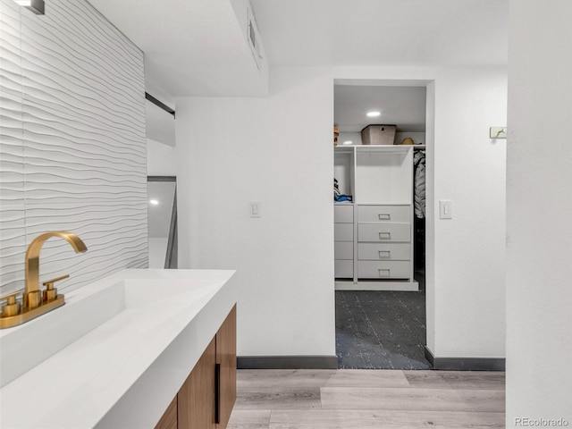 interior space featuring baseboards, a walk in closet, wood finished floors, and vanity