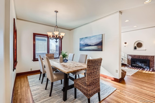 dining room featuring an inviting chandelier, light hardwood / wood-style flooring, crown molding, and a fireplace