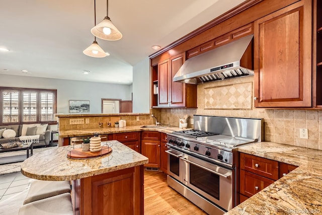 kitchen featuring a kitchen bar, wall chimney range hood, decorative light fixtures, backsplash, and range with two ovens