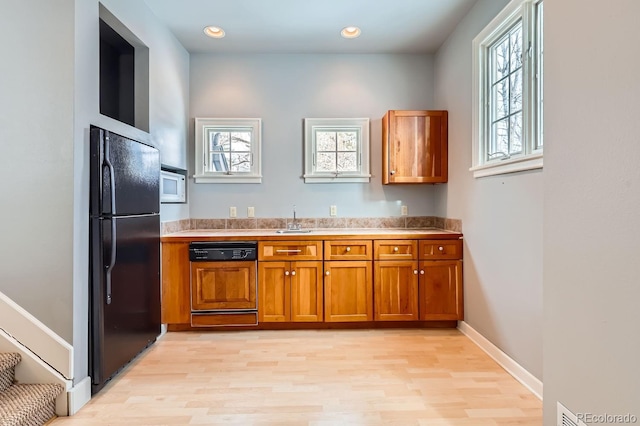 kitchen featuring dishwasher, sink, light wood-type flooring, white microwave, and black fridge