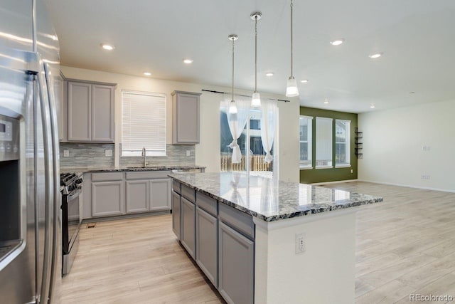 kitchen with a sink, range with gas stovetop, a kitchen island, stainless steel refrigerator with ice dispenser, and gray cabinetry