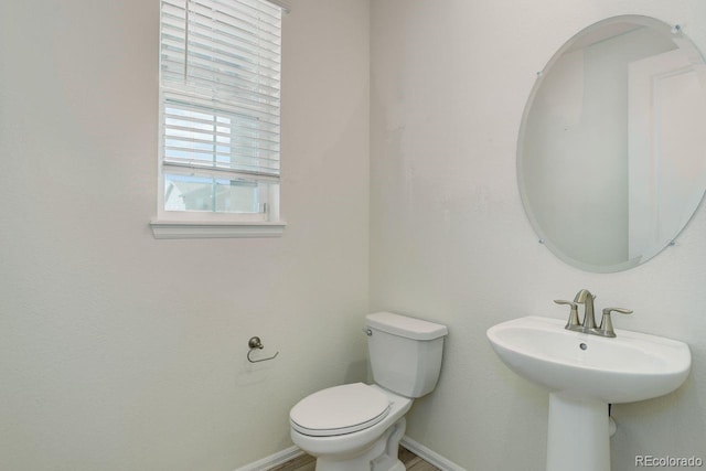 half bath featuring baseboards and toilet