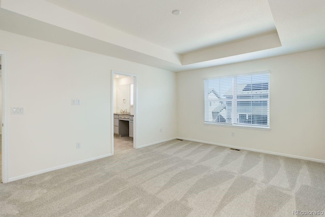 empty room featuring baseboards, a tray ceiling, and light carpet