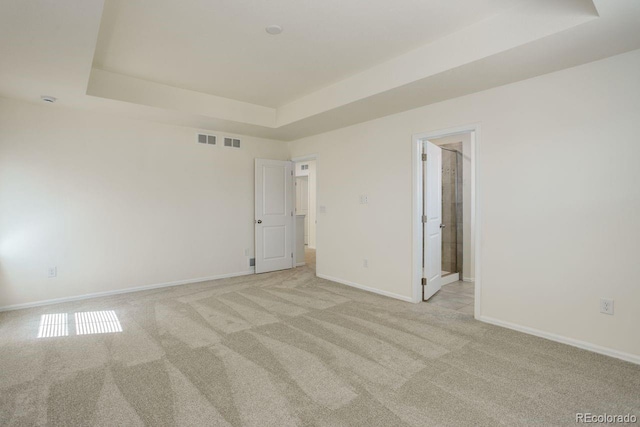 unfurnished room featuring baseboards, a tray ceiling, light carpet, and visible vents