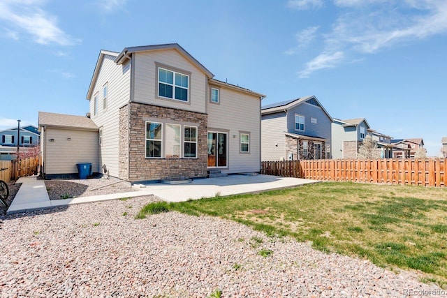 back of property with a lawn, a residential view, a fenced backyard, a patio, and stone siding