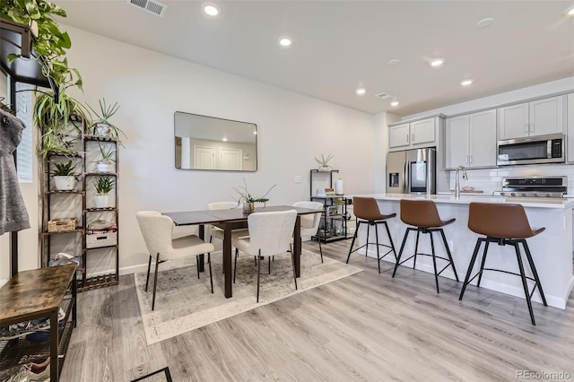 kitchen featuring appliances with stainless steel finishes, light hardwood / wood-style flooring, tasteful backsplash, sink, and a kitchen breakfast bar