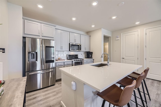 kitchen with appliances with stainless steel finishes, tasteful backsplash, sink, light hardwood / wood-style floors, and a kitchen island with sink