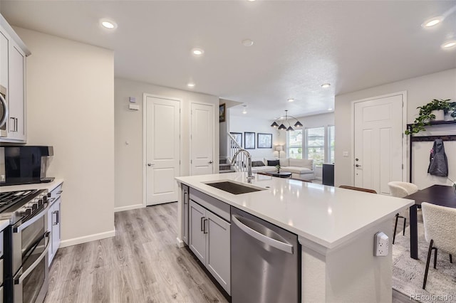 kitchen featuring appliances with stainless steel finishes, light wood-type flooring, sink, and a kitchen island with sink