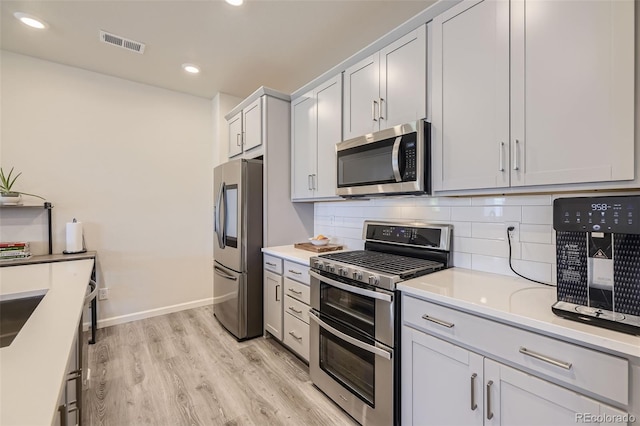 kitchen featuring light hardwood / wood-style floors, appliances with stainless steel finishes, white cabinets, and tasteful backsplash