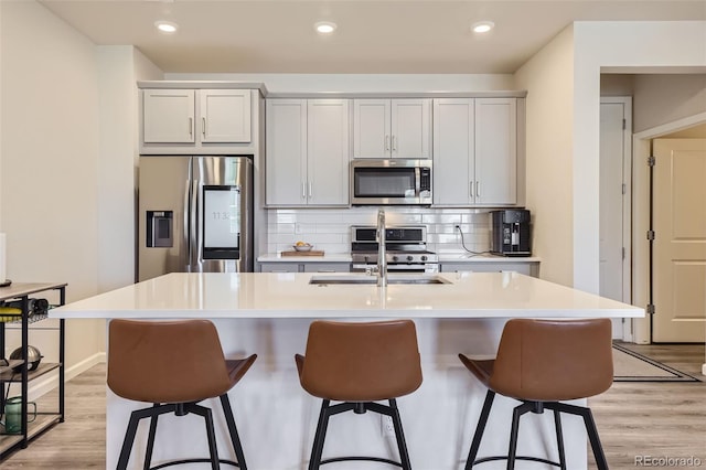 kitchen featuring tasteful backsplash, light wood-type flooring, an island with sink, appliances with stainless steel finishes, and a kitchen breakfast bar