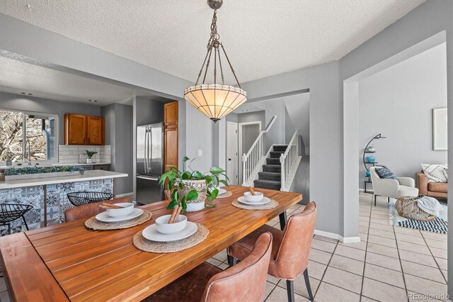 dining room with light tile patterned floors, a textured ceiling, stairs, and baseboards