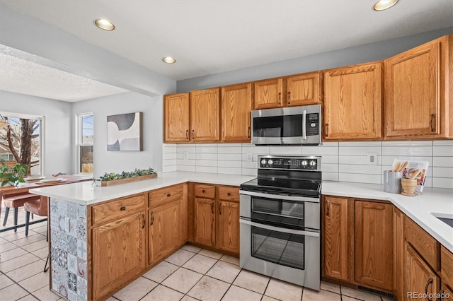 kitchen with stainless steel appliances, a peninsula, visible vents, light countertops, and decorative backsplash