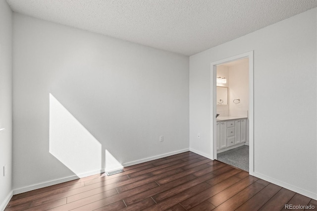 unfurnished bedroom featuring a textured ceiling, dark wood-style flooring, connected bathroom, and baseboards