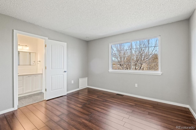 unfurnished bedroom featuring visible vents, a textured ceiling, baseboards, and wood finished floors