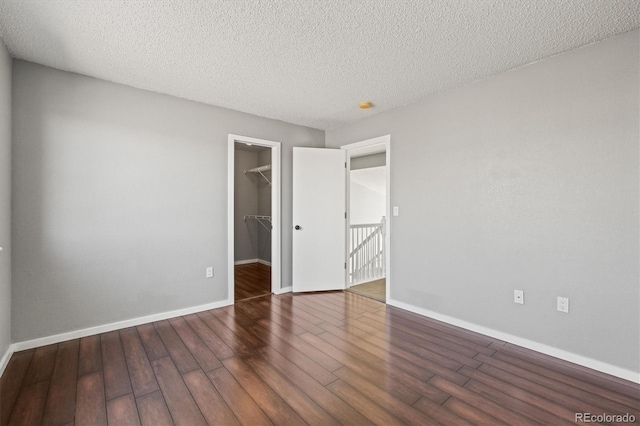 unfurnished bedroom with a walk in closet, a textured ceiling, baseboards, and wood finished floors