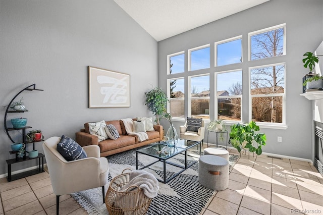 tiled living room featuring baseboards, high vaulted ceiling, and a glass covered fireplace