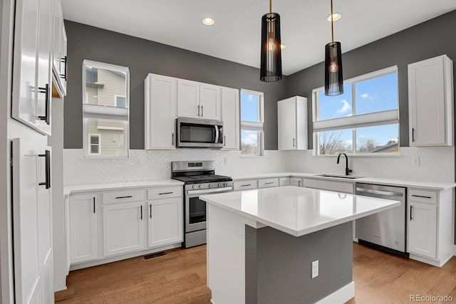 kitchen with appliances with stainless steel finishes, a kitchen island, sink, and white cabinets