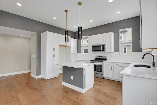 kitchen with appliances with stainless steel finishes, sink, white cabinetry, a kitchen island, and hanging light fixtures