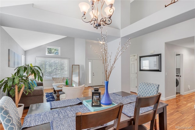 dining room featuring washer / dryer, high vaulted ceiling, a notable chandelier, and hardwood / wood-style flooring