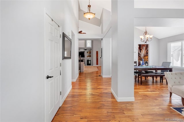 hall with light hardwood / wood-style floors, high vaulted ceiling, and an inviting chandelier