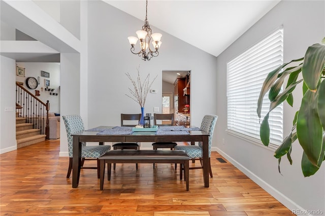 dining space with high vaulted ceiling, an inviting chandelier, and light hardwood / wood-style flooring