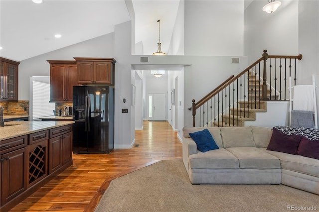 kitchen featuring backsplash, high vaulted ceiling, dark wood-type flooring, black refrigerator with ice dispenser, and decorative light fixtures