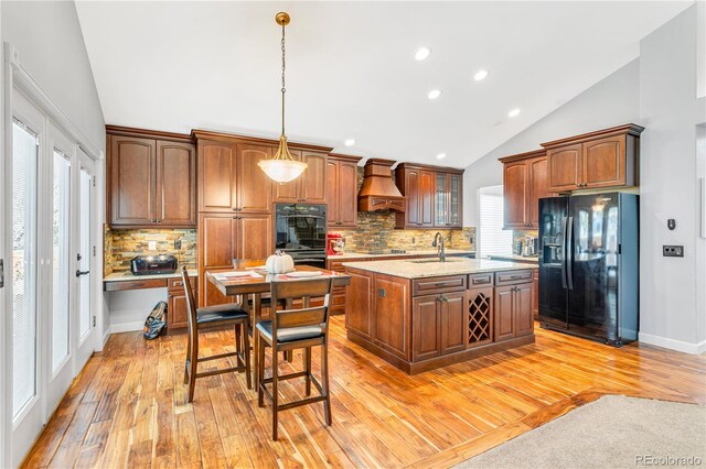 kitchen with lofted ceiling, premium range hood, black appliances, light wood-type flooring, and a healthy amount of sunlight