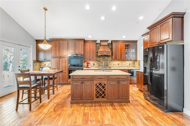 kitchen with custom exhaust hood, black appliances, light hardwood / wood-style floors, hanging light fixtures, and lofted ceiling