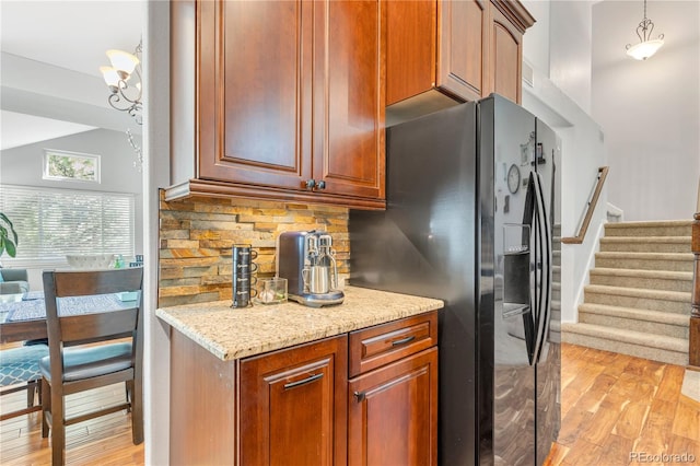 kitchen with black fridge, hanging light fixtures, light wood-type flooring, tasteful backsplash, and light stone counters