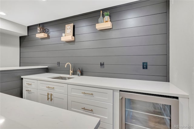 bar featuring white cabinetry, sink, beverage cooler, and wood walls