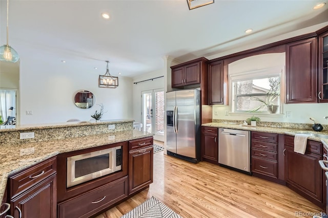 kitchen with light stone counters, stainless steel appliances, decorative light fixtures, and light hardwood / wood-style flooring