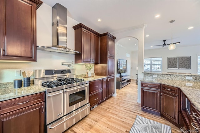 kitchen with range with two ovens, ceiling fan, light hardwood / wood-style floors, light stone countertops, and wall chimney range hood