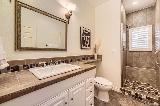 bathroom featuring vanity, toilet, a tile shower, and decorative backsplash