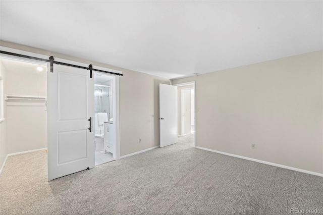 unfurnished bedroom featuring a closet, ensuite bathroom, light colored carpet, and a barn door