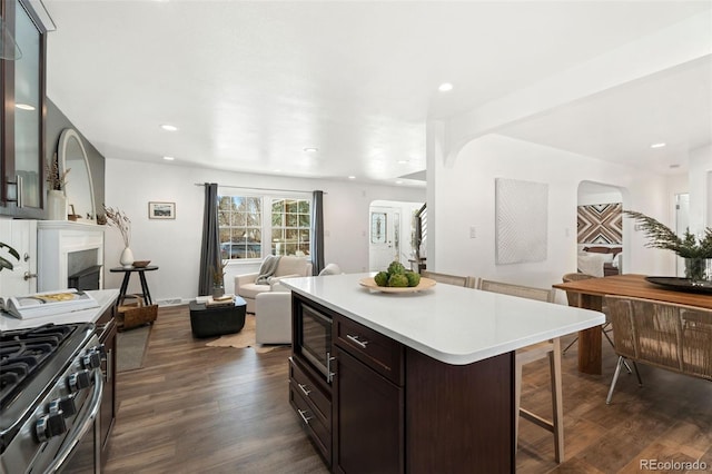 kitchen with built in microwave, a center island, dark brown cabinets, dark hardwood / wood-style floors, and stainless steel stove