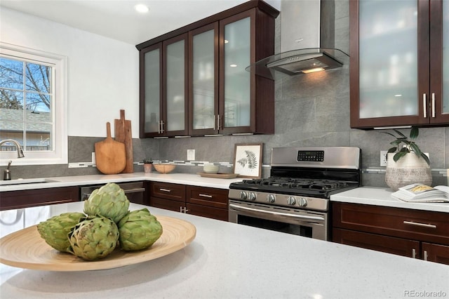 kitchen with wall chimney range hood, sink, backsplash, dark brown cabinets, and stainless steel appliances