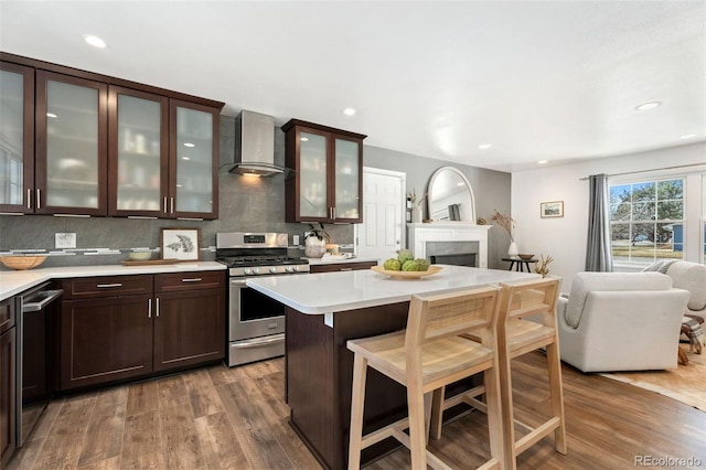 kitchen with decorative backsplash, wall chimney exhaust hood, wood-type flooring, and stainless steel gas range oven