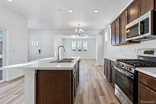 kitchen featuring sink, appliances with stainless steel finishes, a kitchen island with sink, dark brown cabinetry, and decorative light fixtures