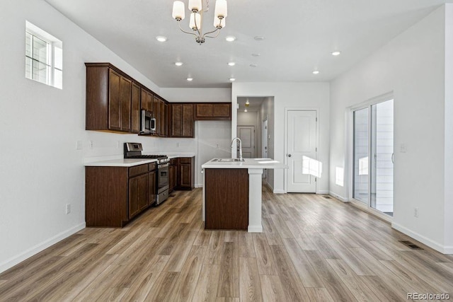 kitchen featuring a kitchen island with sink, pendant lighting, light wood-type flooring, and appliances with stainless steel finishes