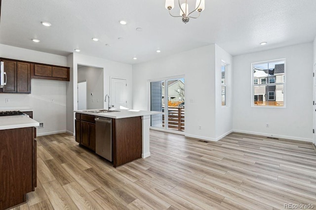 kitchen featuring appliances with stainless steel finishes, decorative light fixtures, an island with sink, sink, and light hardwood / wood-style floors