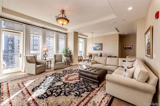 living room with wood-type flooring, a tray ceiling, and plenty of natural light