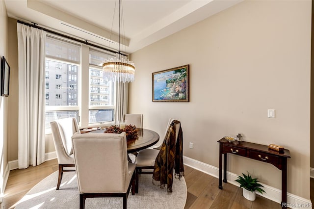 dining space featuring light hardwood / wood-style floors, a notable chandelier, and a raised ceiling