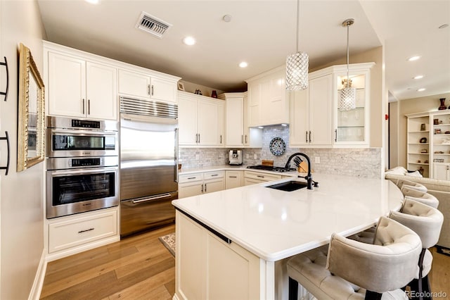 kitchen with light hardwood / wood-style flooring, kitchen peninsula, hanging light fixtures, stainless steel appliances, and a breakfast bar