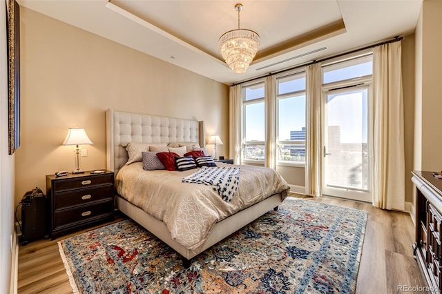 bedroom featuring a chandelier, light hardwood / wood-style flooring, and a tray ceiling