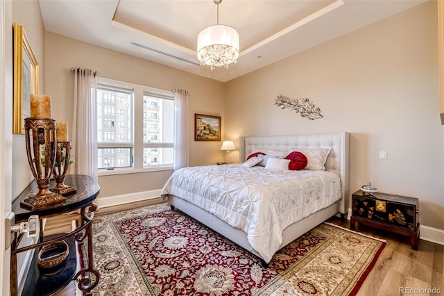 bedroom with an inviting chandelier, a tray ceiling, and light hardwood / wood-style floors