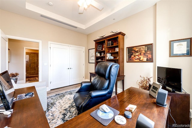 home office featuring hardwood / wood-style floors, ceiling fan, and a raised ceiling